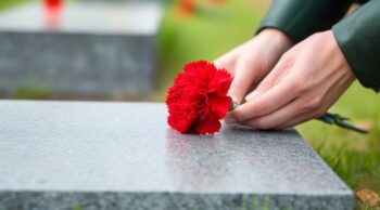 Entenda por que visitar túmulos ajuda a superar o luto Mãos depositam delicadamente um cravo vermelho sobre uma lápide de granito, incentivando o ato de visitar túmulos.